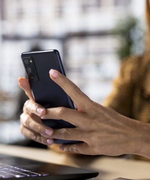 Professional woman checking her smartphone for business emails and project updates while multitasking at her desk. Female executive employs mobile technology to meet deadlines. Close up.